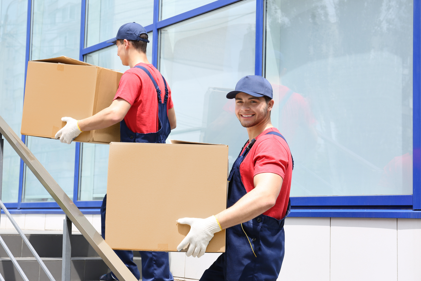 Two Male Workers Carrying Boxes on Staircases